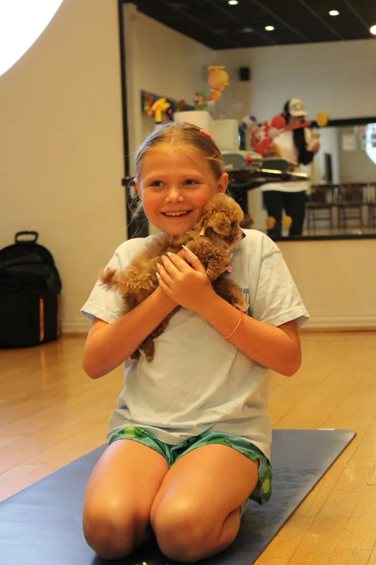 Young guest kneeling on a yoga mat with an apricot puppy at Pawty Yoga Houston