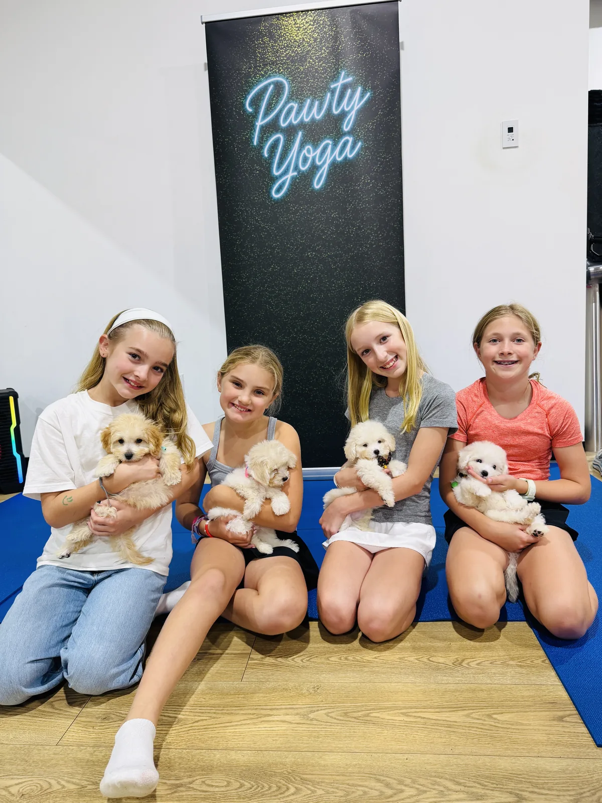Tween friends holding puppies under the Pawty Yoga neon sign at a Houston party