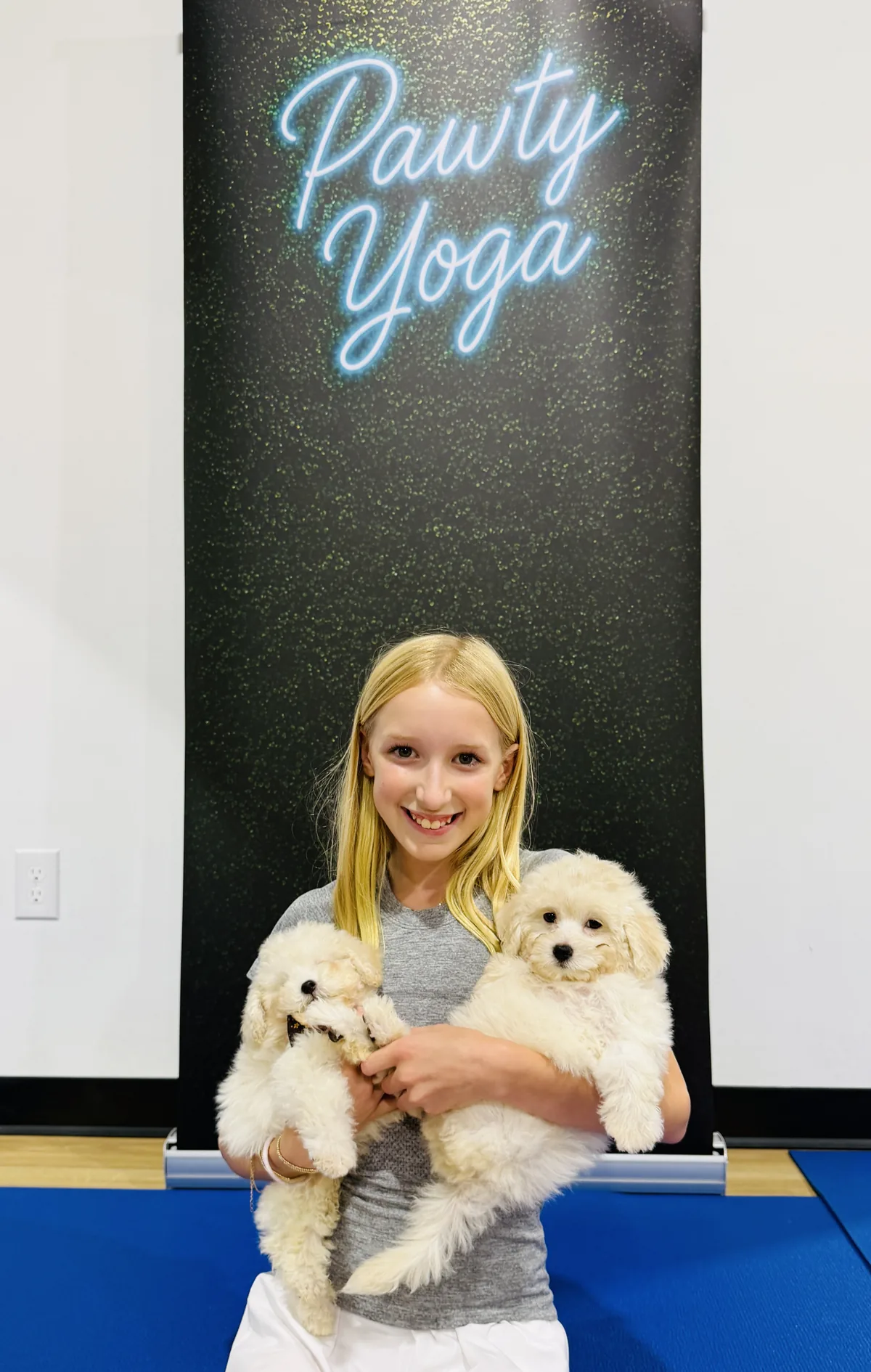 A girl holding two puppies under the Pawty Yoga sign in Houston
